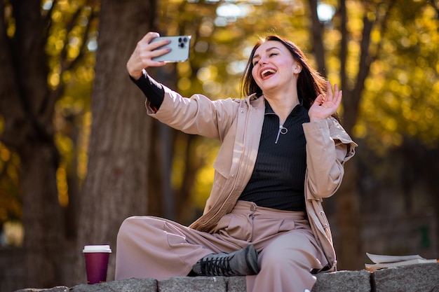 Feliz retrato de mulher estilosa no outono com sobretudo ela está tirando uma selfie