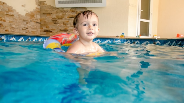 Feliz riendo y sonriente niño jugando con juguetes y aprendiendo a nadar en la piscina interior