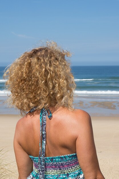 Feliz rubia de pie en el mar posando en un día soleado