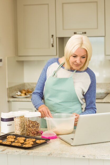Feliz rubia preparando masa siguiendo la receta en línea