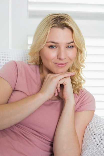 Feliz rubia relajante en el sofá sonriendo a la cámara