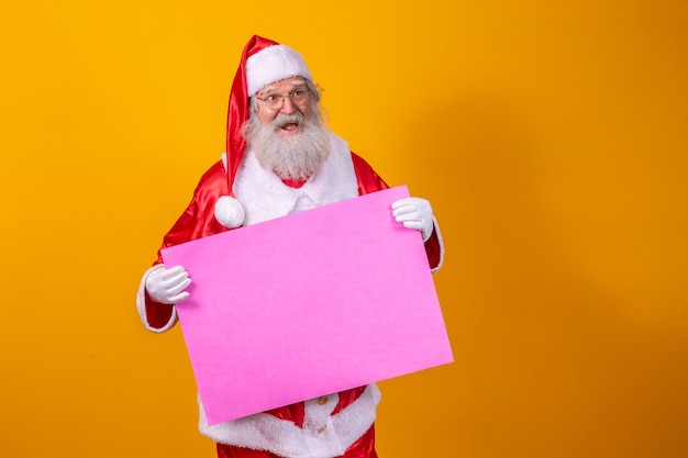 Feliz Santa Claus sosteniendo un tablero en blanco aislado sobre fondo amarillo con espacio de copia.