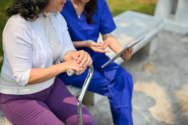 Feliz senhora asiática com deficiência olhando para a tela de um tablet e conversando com seu cuidador