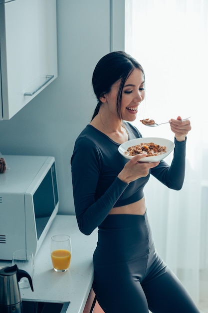 Feliz senhora desportiva com uma tigela de cereais e uma colher perto do armário da cozinha