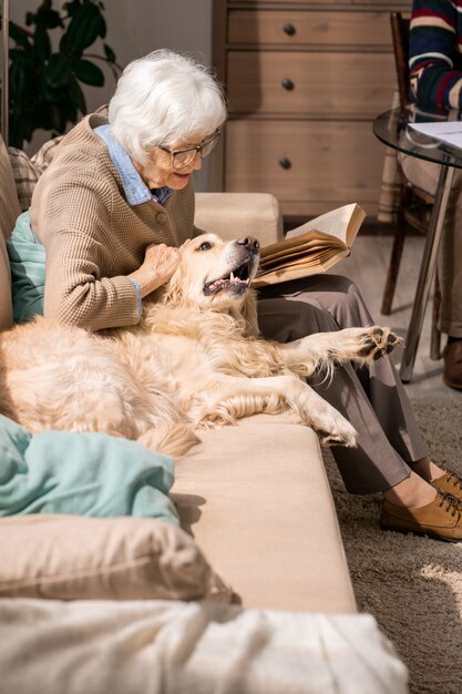 Feliz senhora sênior carinhos com cachorro no sofá