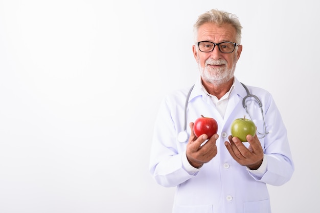 Feliz senior hombre barbudo doctor sonriendo mientras sostiene la manzana roja y manzana verde sobre blanco