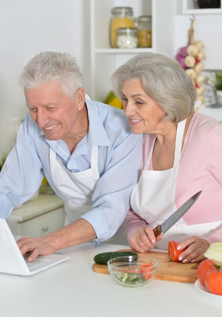 Feliz senior hombre y mujer en la cocina con portátil