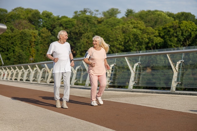 Feliz senior hombre y mujer corren juntos a lo largo de la pasarela en verano