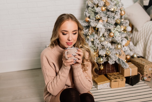 Feliz señorita con cabello largo cerca de la chimenea y el árbol de Navidad