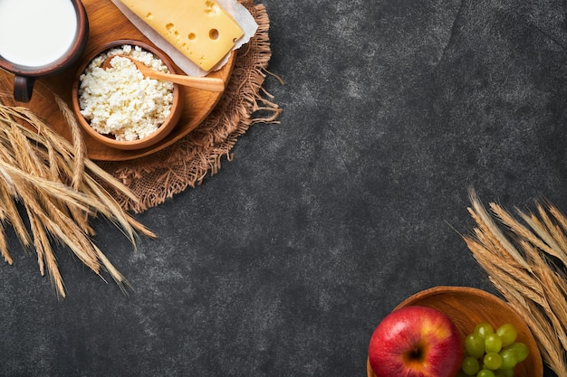 Feliz Shavuot Antecedentes para la celebración judía religiosa tradicional de Shavuot Leche y queso trigo maduro y frutas Productos lácteos sobre fondo gris oscuro antiguo Concepto de Shavuot Vista superior Mock up