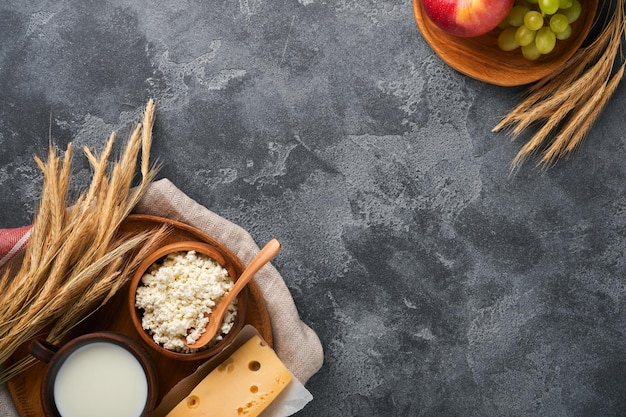 Feliz Shavuot Antecedentes para la celebración judía religiosa tradicional de Shavuot Leche y queso trigo maduro y frutas Productos lácteos sobre fondo gris oscuro antiguo Concepto de Shavuot Vista superior Mock up