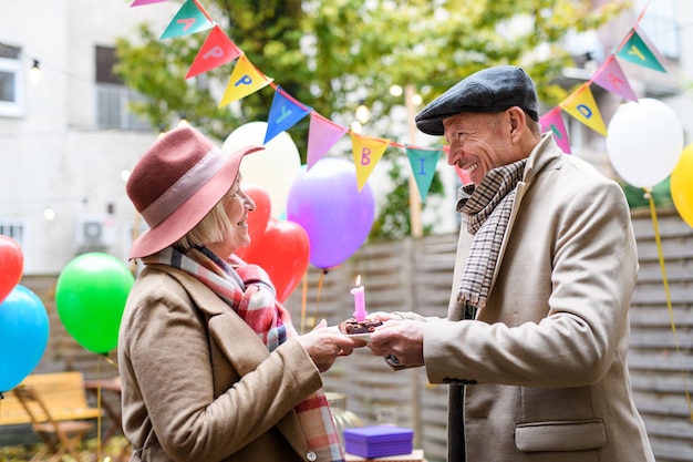 Un feliz socios senior en un café al aire libre en la ciudad, pareja celebrando un cumpleaños. Concepto de coronavirus.