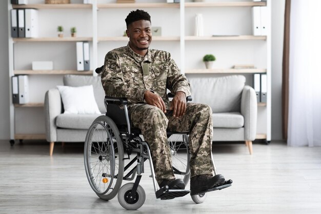Feliz soldado negro sentado no interior da clínica de cadeira de rodas