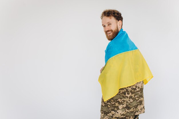 Feliz soldado patriota ucraniano con uniforme militar sosteniendo una bandera amarilla y azul en un fondo blanco