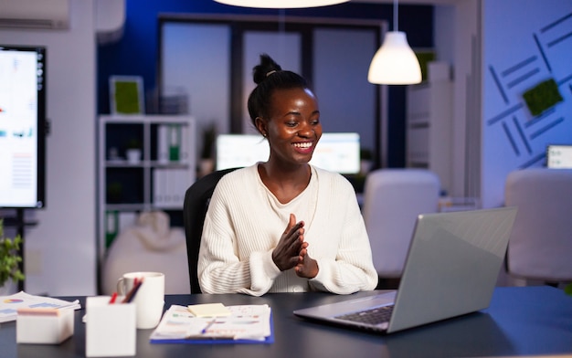 Feliz sonriente africana debido a los resultados positivos trabajando lat por la noche en la oficina de negocios