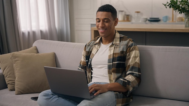 feliz sonriente afroamericano hombre étnico trabajando en casa distante trabajo en línea estudiando en el sofá tipo