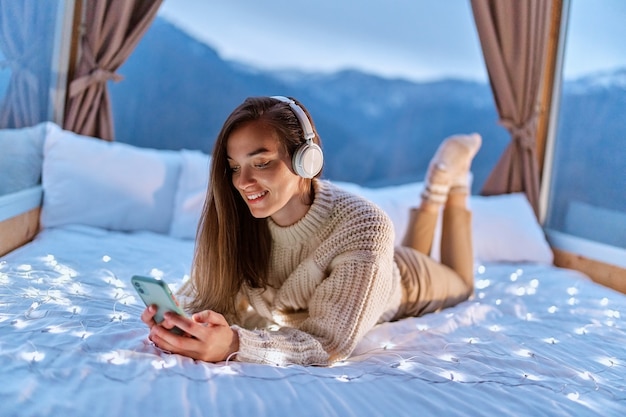 Feliz sonriente alegre mujer despreocupada satisfecha con auriculares y teléfono para ver videos en línea