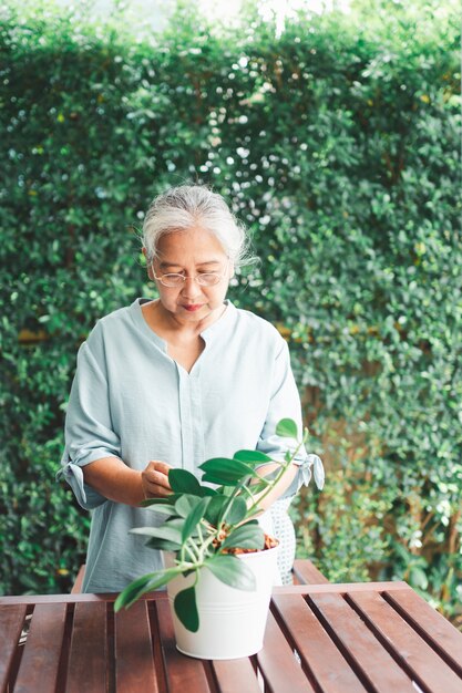 Feliz y sonriente anciana asiática plantar flores en maceta