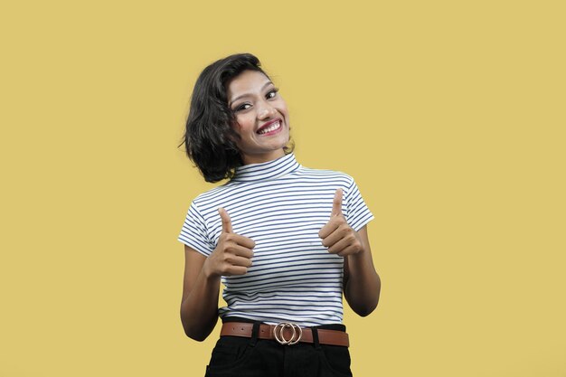 Foto feliz sonriente encantadora mujer joven mostrando los pulgares hacia arriba sobre fondo amarillo mirando a la cámara