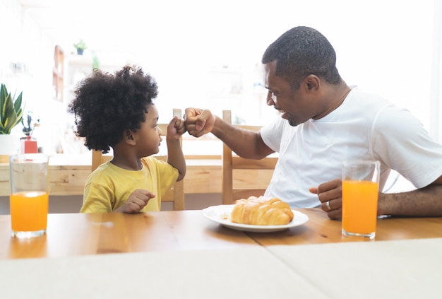 Feliz sonriente familia afroamericana chocando el puño mientras desayunaba en la mesa en casa juntos Familia disfruta de la comida Feliz día del padre