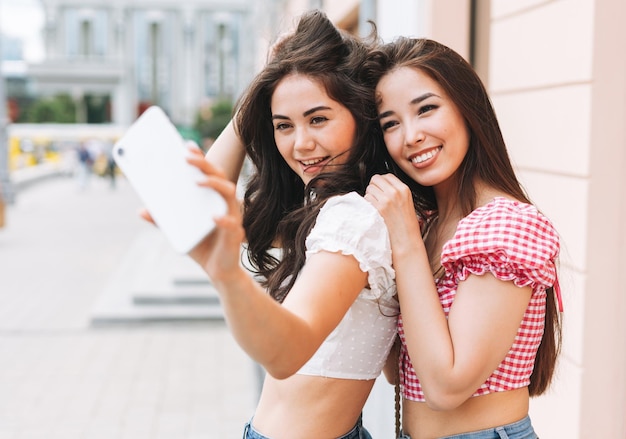 Feliz sonriente hermosa morena joven amiga en ropa de verano tomando selfie en teléfono móvil