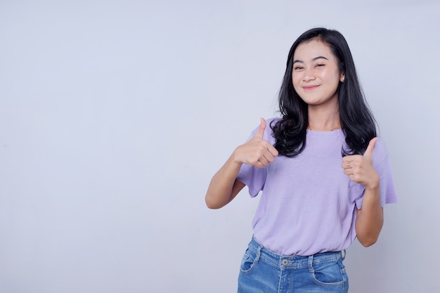 Feliz sonriente hermosa mujer mostrando el pulgar hacia arriba, que le gusta aprobar una idea impresionante en la pared blanca clara