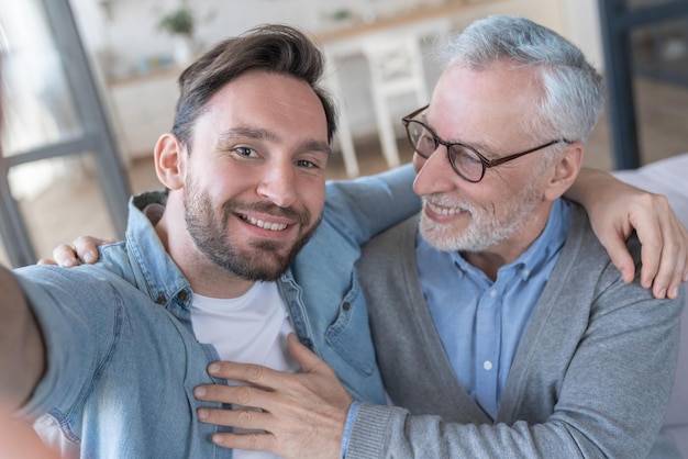 Feliz y sonriente hijo adulto tomando una selfie con su anciano padre.