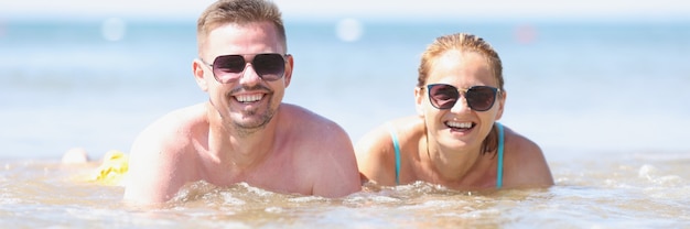 Feliz sonriente hombre y mujer con gafas de sol se encuentran en la orilla del mar