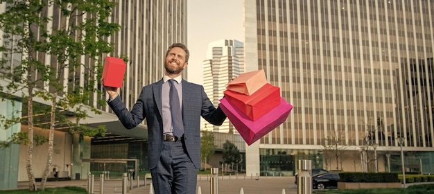 Feliz sonriente hombre de negocios maduro en traje sostiene paquetes y caja de regalo fuera del descuento de la oficina