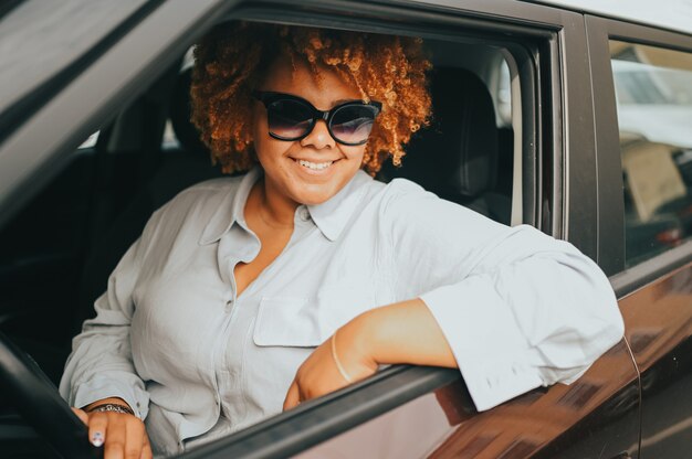 Feliz sonriente joven afroamericana conductor de pelo rojo afro en gafas de sol sentado en nuevo