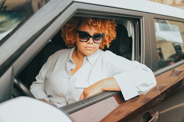 Feliz sonriente joven afroamericana conductor de pelo rojo afro en gafas de sol sentado en nuevo