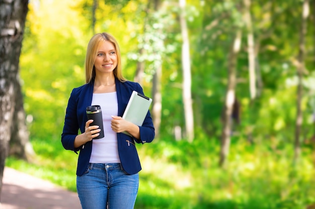 Feliz sonriente joven caucásica exitosa niña adulta caminando en el parque con tableta y teléfono