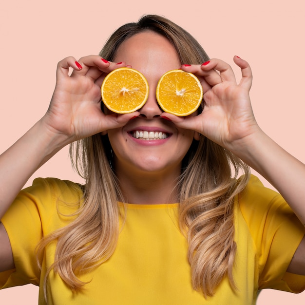 Feliz y sonriente joven jugando con una naranja cortada por la mitad y delante de sus ojos.