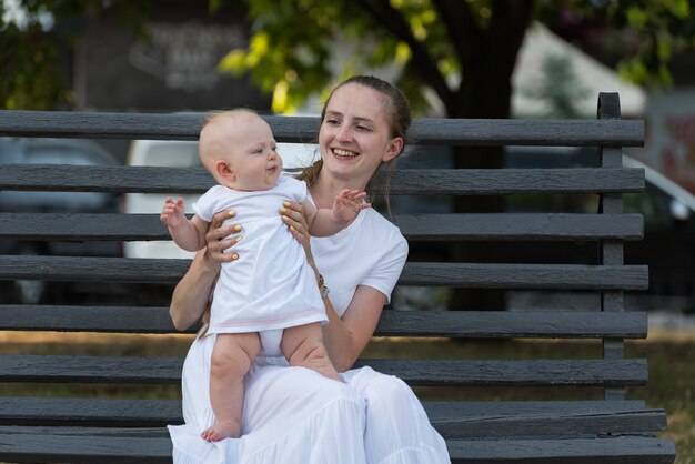 Feliz sonriente joven madre con bebé sentado en un banco