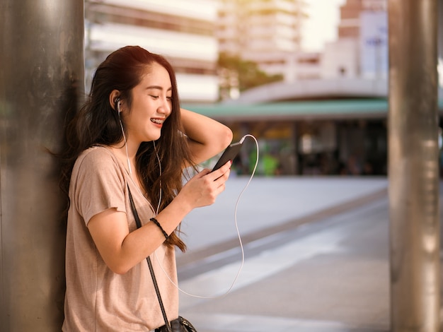 Feliz sonriente joven mujer asiática escucha música en auriculares y con smartphone.