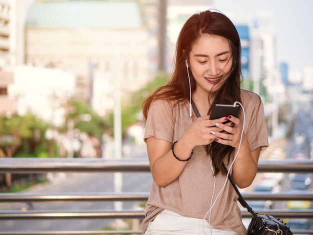 Feliz sonriente joven mujer asiática escucha música en auriculares y con smartphone.