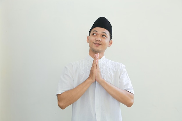 Feliz sonriente joven musulmán asiático vestido con traje árabe de pie con gestos de saludo de Eid Mubarak