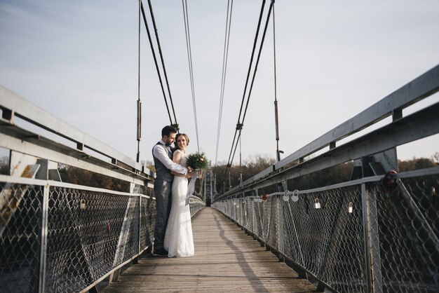 Feliz sonriente joven novia y el novio están de pie en el puente colgante