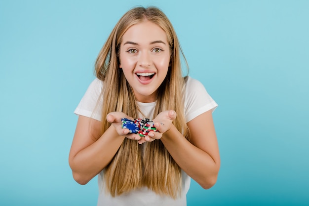 Feliz sonriente joven rubia con fichas de póker en manos aisladas sobre azul