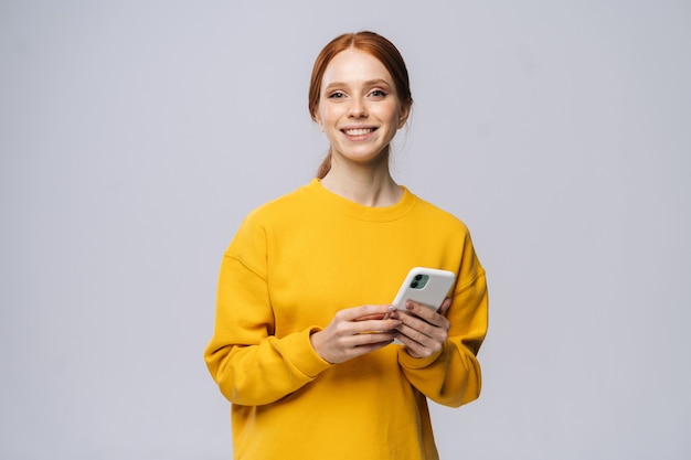 Feliz sonriente joven sosteniendo el teléfono móvil y mirando a la cámara sobre fondo blanco aislado