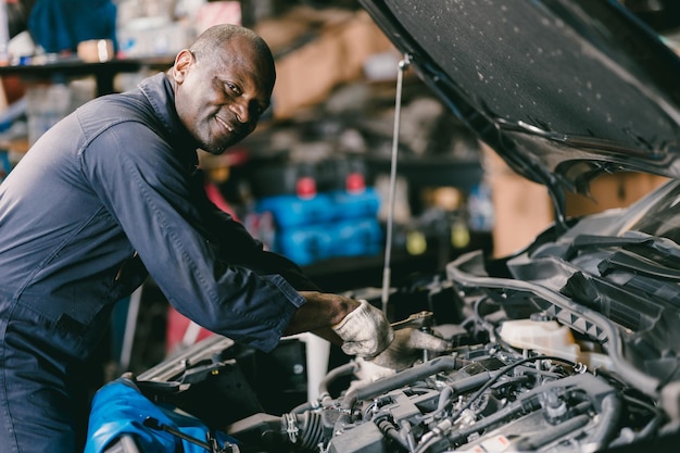 Foto feliz sonriente mecánico masculino servicio de motor de automóvil bajo el capó revisando el reemplazo de aceite en la parte rota en el garaje de automóviles