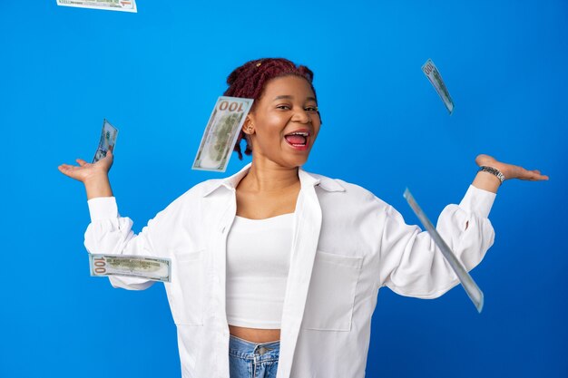 Feliz sonriente mujer afroamericana tirando dinero contra el fondo azul.