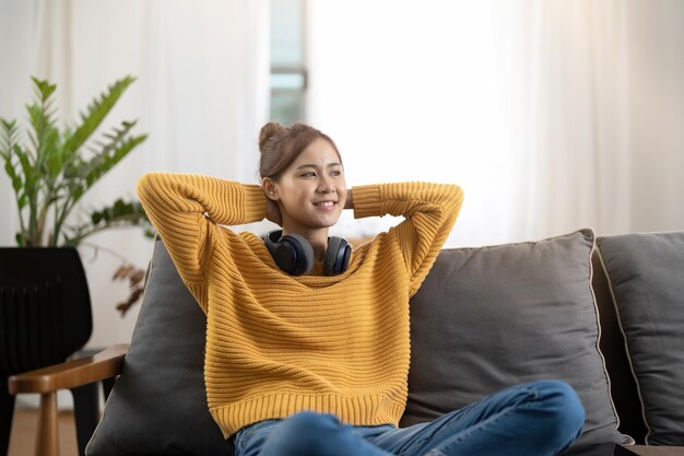 Feliz sonriente mujer joven asiática en auriculares escuchando música acostado en el sofá en casa personas y concepto de ocio