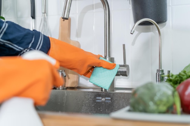 Feliz sonriente mujer joven asiática niña limpieza frota polvo usar trapos botella de spray en el grifo del fregadero en la cocina en casa Higiene doméstica limpieza limpiador personas equipo o herramienta para la limpieza