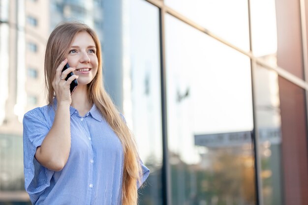 Feliz sonriente mujer joven atractiva llamando por teléfono móvil fuera de la oficina