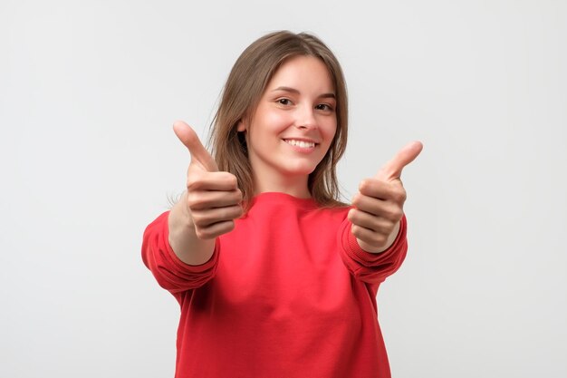 Feliz sonriente mujer joven hermosa que muestra los pulgares arriba gesto