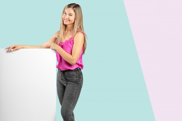 Feliz sonriente mujer joven hermosa en ropa casual elegante rosa que muestra el letrero en blanco o copyspace para lema o texto