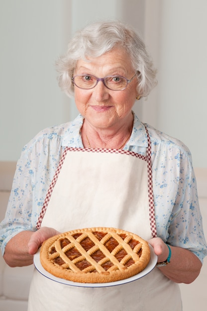 Feliz sonriente mujer mayor mostrando su tarta de albaricoque