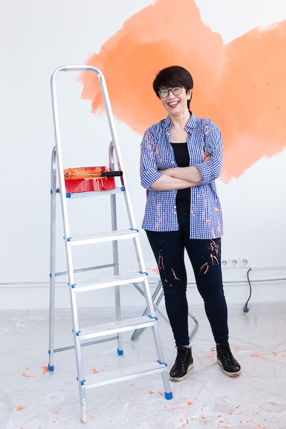 Feliz sonriente mujer de mediana edad pintando la pared interior de la casa nueva. Redecoración, renovación