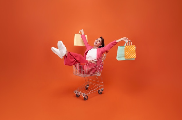 Feliz sonriente mujer de moda con carrito y bolsa de compras caminando promoción de compras venta de verano